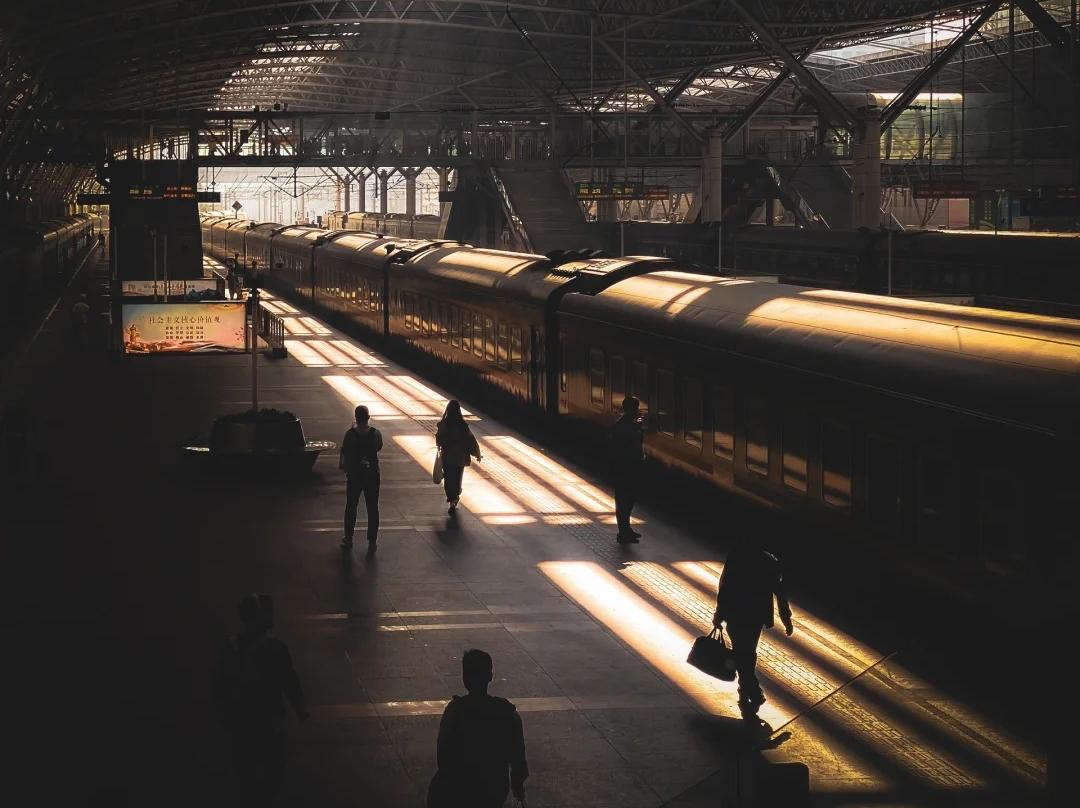 Vintage Passenger Train and Travellers Silhouettes in Sunlit Grand Railway Station Hall