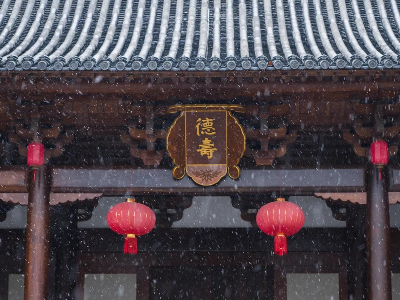 Traditional palace in Hangzhou covered in gentle snow and red lanterns.