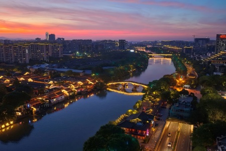Sunset view of Hangzhou Grand Canal, illuminated ancient stone arch bridge and lit waterfront old town buildings