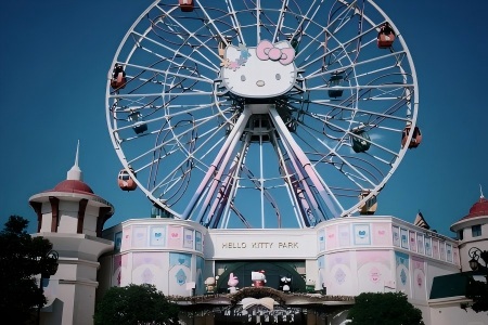Cute pastel Hello Kitty Ferris wheel with colorful cabins above the pastel park entrance building, clear blue sky at Anji Hello Kitty Park in Zhejiang