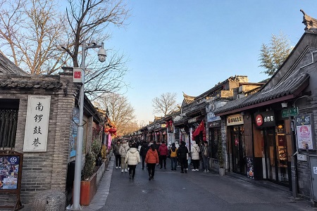 Nanluoguxiang Hutong traditional gray-brick buildings, red lanterns, shops, and visitors walking along the historic street