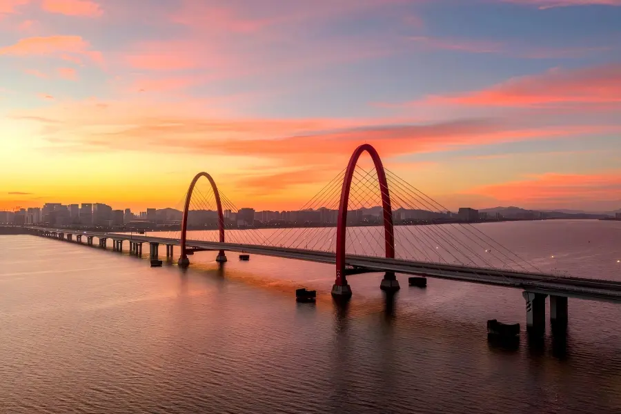 Modern red?arch bridge over Qiantang River under vibrant sunset sky, Hangzhou cityscape