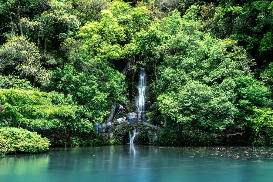 Stone bridge, waterfall and turquoise lake surrounded by thick green woods at Hangzhou Nine?Creeks scenic area