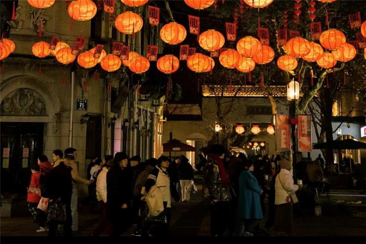 Bustling ancient Hefang Street at night, lined with glowing orange lanterns and crowds of visitors wandering the old pedestrian street in Hangzhou