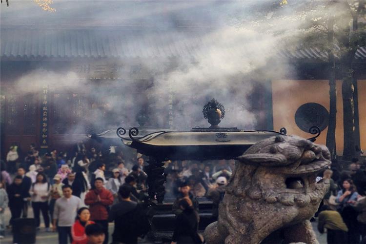 Thick curling incense smoke rising from bronze censer, visitors praying behind stone lion sculpture inside Lingyin Temple, Hangzhou