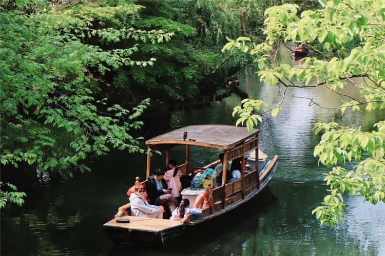 Leisure Wooden Boat Cruise in Green Waterway Tourists sightseeing on traditional wooden boat surrounded by lush green foliage in Hangzhou