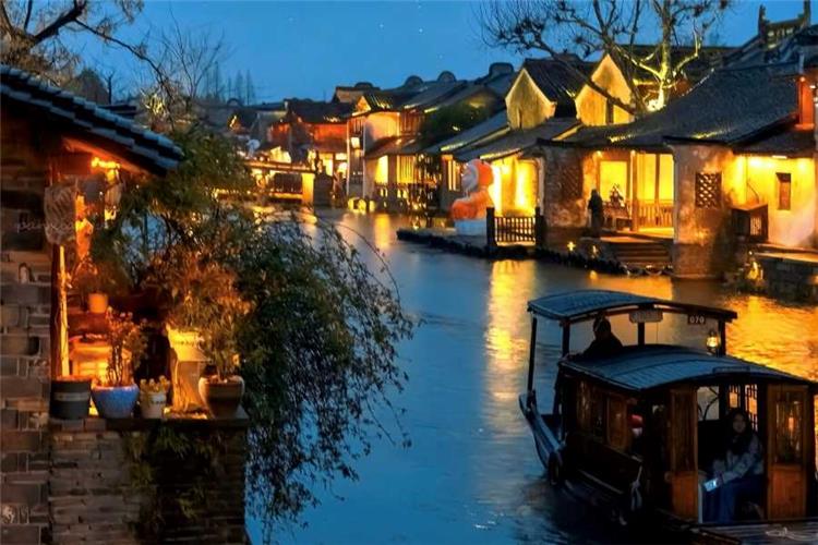 Glowing lantern-lit ancient water town at dusk, wooden boat floating on reflective canal water in Wuzhen Xizha