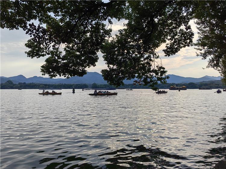West Lake boating in Hangzhou featuring traditional wooden boats drifting on lake water surrounded by rolling green hills and classical lakeside scenery