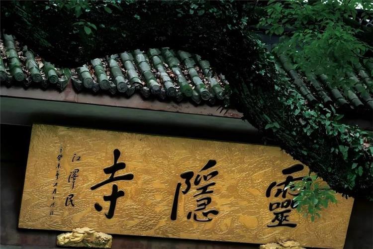 Golden horizontal plaque of Lingyin Temple inscribed with three bold Chinese calligraphy characters, framed by ancient green tile eaves and lush overhanging green branches, full of solemn tranquil Zen atmosphere of millennium Buddhist temple