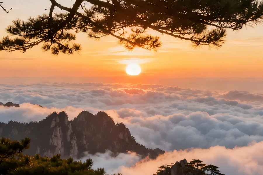 Sunrise at Mount Huangshan in Anhui showing golden sunrise glow spilling over jagged granite peaks, floating sea of clouds and iconic twisted Huangshan pine silhouettes, a world-famous mountain sunrise landscape
