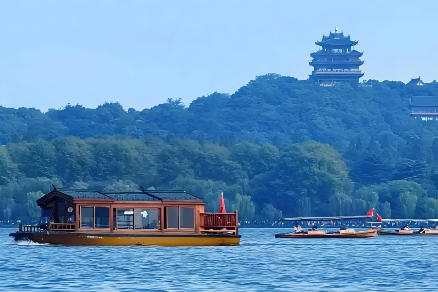 Antique painted pleasure boats cruising West Lake, with Leifeng Pagoda and Su Causeway visible across the reflective lake surface