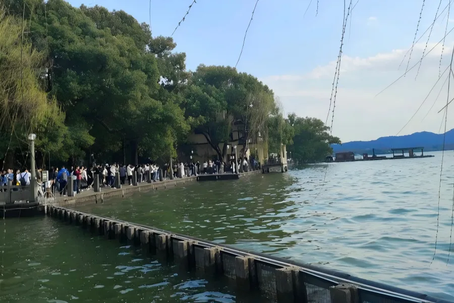 West Lake Lakeside in Hangzhou showing visitors wandering tree-lined causeway beside rippling lake waters