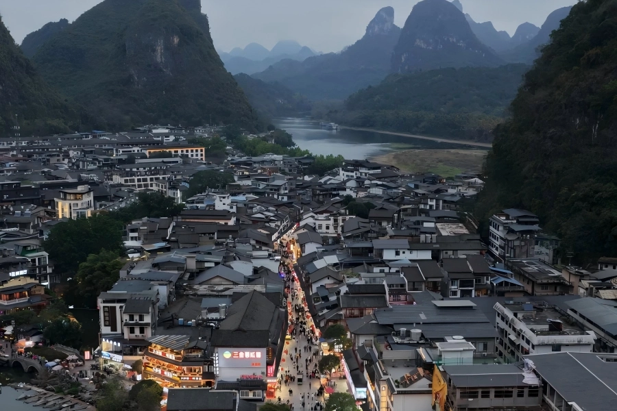 Yangshuo West Street in Guilin showing bustling pedestrian scene along grey?brick old street, framed by distant Guilin karst hill peaks