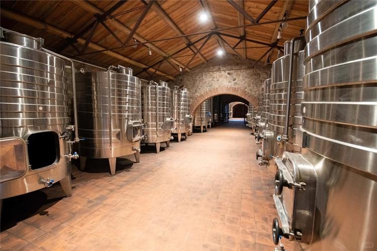 Rows of large stainless steel wine fermentation tanks inside stone?wall winery production facility