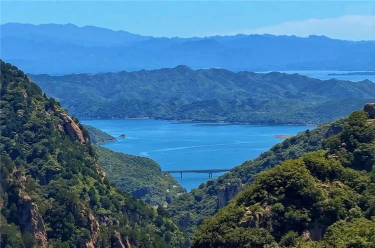 Wide mountain landscape of Beijing Heilongtan scenic area with blue reservoir lake, layered mountain ranges and bridge