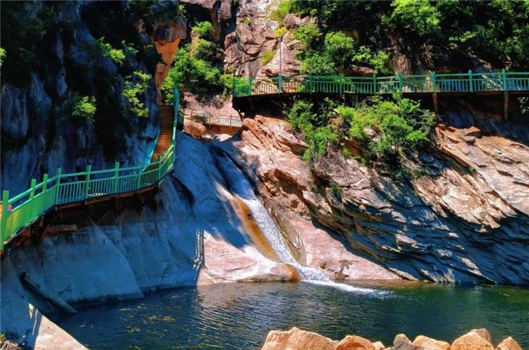 Mountain waterfall dropping into green pool beside green?railed cliff boardwalk in Heilongtan canyon