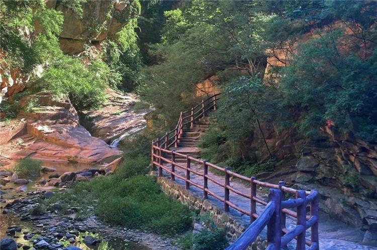 Stone hiking path with wooden railings along rocky stream valley at Beijing Heilongtan scenic spot