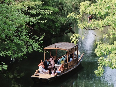 Tourists taking wooden boat trip surrounded by lush green trees in Hangzhou