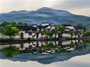 Scenic view of Hongcun Village Anhui, white Huizhou architecture reflected in calm lake with misty mountains backdrop