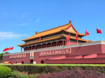 Iconic Tiananmen Gate with red walls, golden roof and red flags under clear blue sky