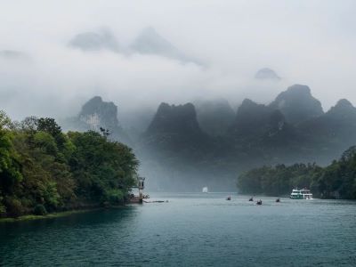 Mist-shrouded karst peaks along Li River in Guilin, green river with cruise boats and fishing rafts