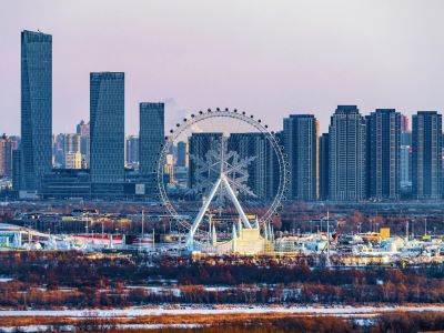 Snowflake-themed ferris wheel at Harbin Ice and Snow World with modern city high-rise buildings in background