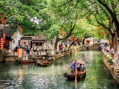 Ancient Tongli water town in Suzhou, stone canals, wooden paddle boat, old white-walled houses and red lanterns under green trees