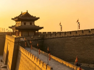 Ancient tower building on Xi'an City Wall bathed in warm golden sunset light with red lanterns and flags
