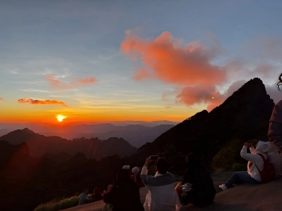 Tourists watching stunning sunrise over layered peaks of Huangshan Mountain, glowing orange morning sky