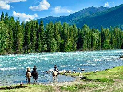 Kanas River in Xinjiang with forests, mountains, turquoise water, and horseback riders by the riverside