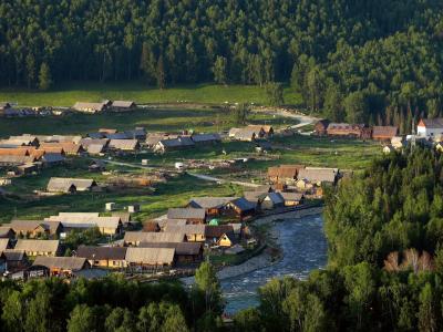 Hemu Village in Xinjiang with wooden houses, a river valley, and forest-covered mountains in the Altai region