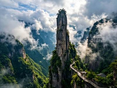 Enshi Grand Canyon in Hubei with towering sandstone peaks, misty clouds, green cliffs, and a scenic cliffside walkway
