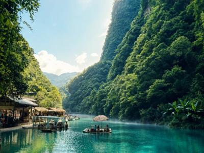 Pingshan Canyon in Enshi, Hubei with crystal clear turquoise water, green mountains, forests, and traditional boat rides