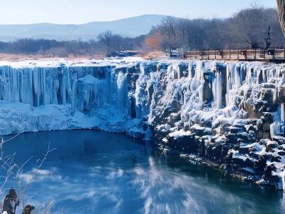 Winter view of Jingpo Lake with frozen waterfall, snow-covered cliffs and icy blue water