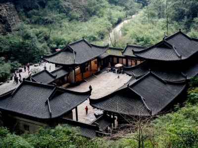 Ancient Chinese post house hidden in karst valley, traditional courtyard buildings surrounded by green mountains, Wulong Karst China