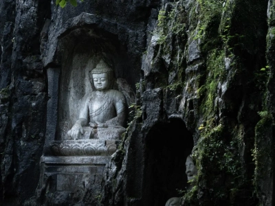 Ancient stone Buddha statue nestled in mossy rocky cliff, serene Buddhist grotto art in Zhejiang China