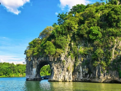 Natural karst rock arch by river, Elephant Trunk Hill landmark in Guilin, lush green trees, blue sky