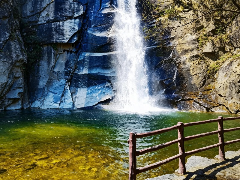 Spectacular mountain waterfall plunging into clear turquoise pool surrounded by steep rock cliffs in Heilongtan