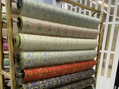 Rolled silk fabrics with traditional patterns displayed on metal racks inside a silk shop